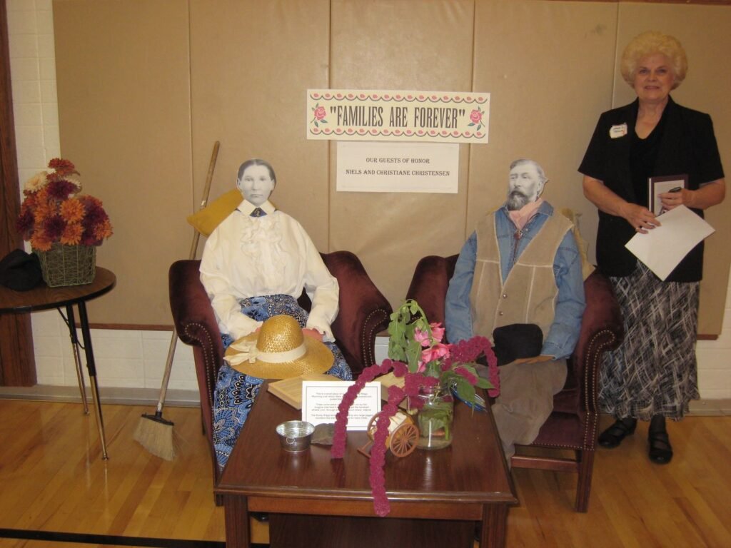 Two life-size cutout figures of Niels and Christiane seated in chairs beneath a banner reading Families Are Forever